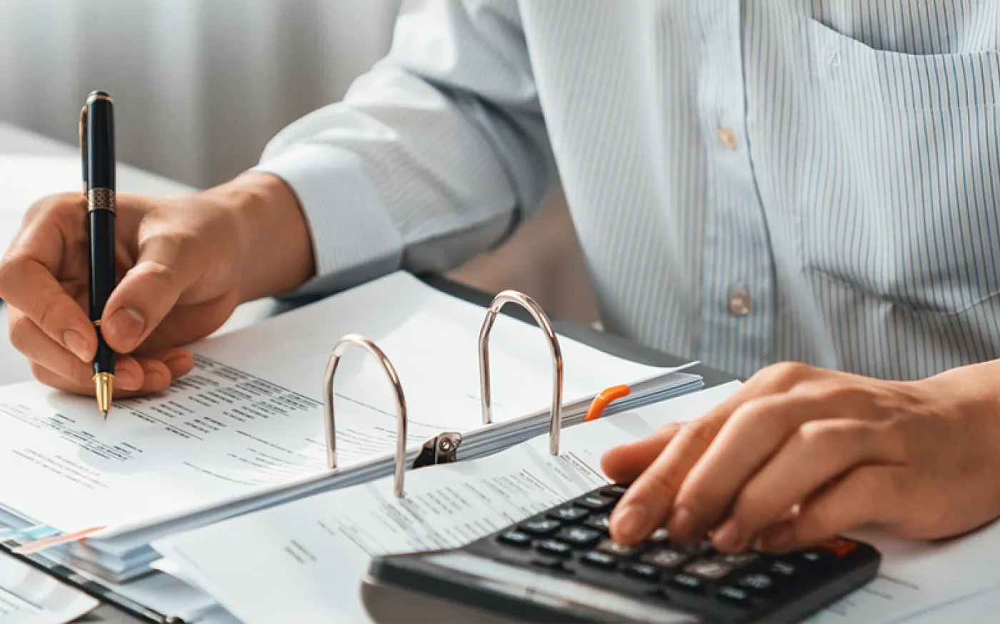 A person at a desk, using a calculator and writing in a notebook.